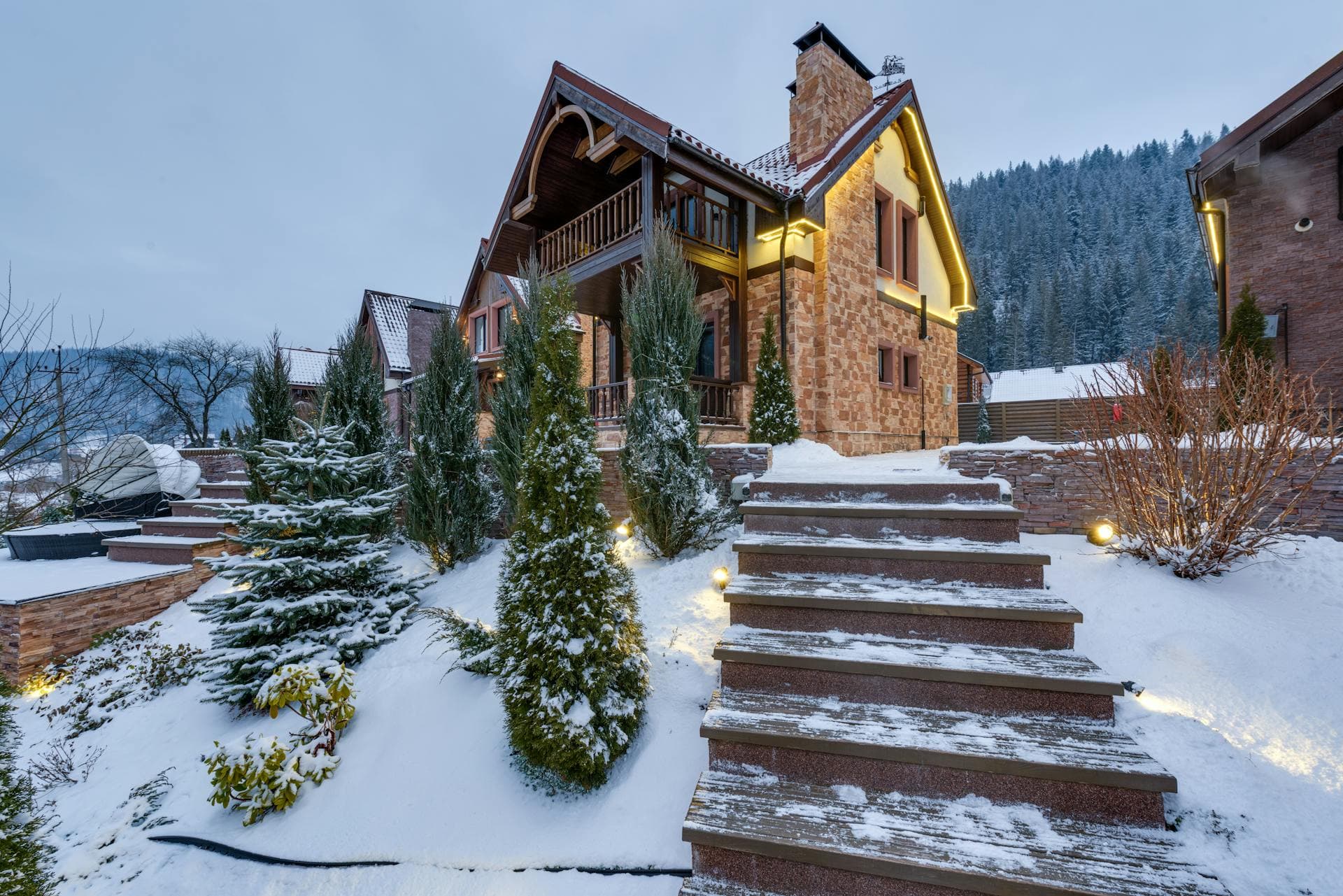 A luxury stone mountain chalet dusted with snow, framed by pines and lit stone steps — the caliber of Park City home Assured Properties has kept spotless since 1985.